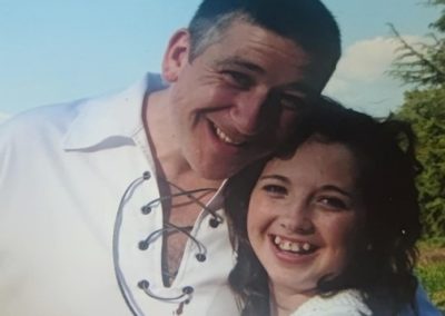 Laura as a child with her dad - A man and child hug in the sunshine.