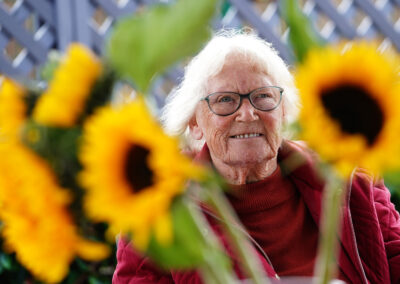 A woman (Margaret) smiles amongst sunflowers.