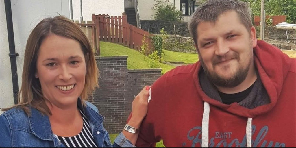 A woman (Susan Colin, Housing Support Manager) and a man (Stuart), standing side by side and smiling brightly.