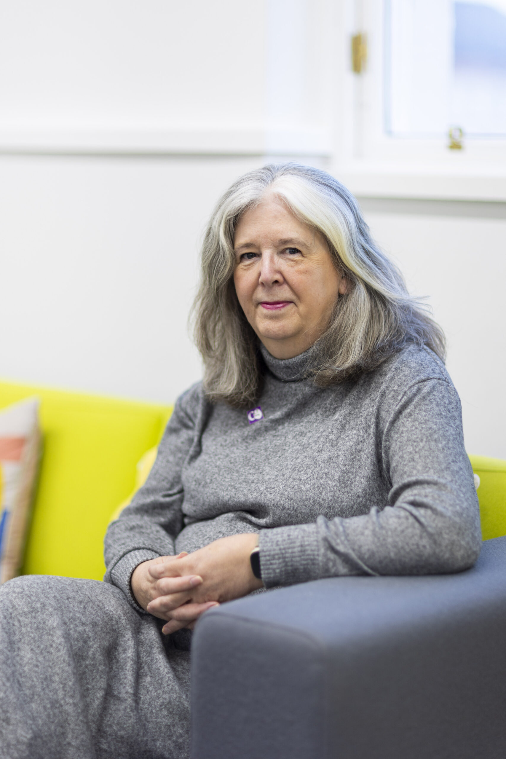 A woman (Lucy) looks towards the camera while sitting on a grey and lime green sofa.