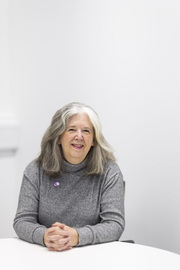 A woman (Lucy) smiles towards the camera while leaning on a white table.