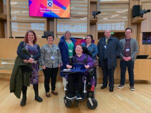 A group of people smile at the camera. They are in the Scottish Parliament.