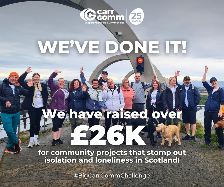 A group of people and 2 dogs stand in front of the Falkirk Wheel, waving at the camera. The text says 'We've done it! We have raised over £26k for community projects that stomp out isolation and loneliness in Scotland #BigCarrGommChallenge' 