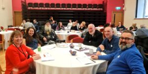 Group of 6 people sat around a table in a hall.