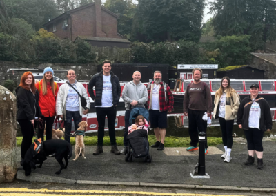 A group photo of ten people and two dogs standing in front of canal boats