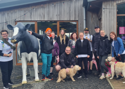 Eleven people and two dogs pose with a statue of a cow outside of 'The Milk Barn' in Falkirk