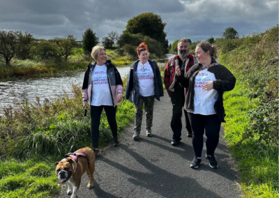 Four people and a dog walk along a canal in the sunshine