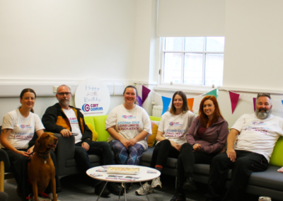 An image of six people and a dog sitting on a sofa in Carr Gomm fundraising t-shirt's which read 'Stomping out isolation and loneliness'