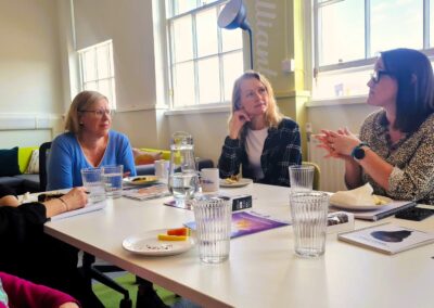 Four women are at a table. One is talking while the others are looking engaged.