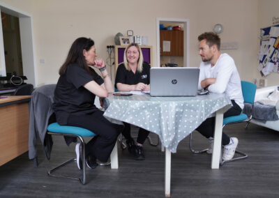 Two women and a man sitting around a table with a laptop. Carr Gomm