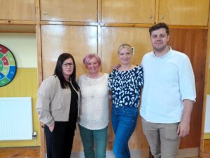 Four people standing together and smiling against a wood panelled background. | Carr Gomm