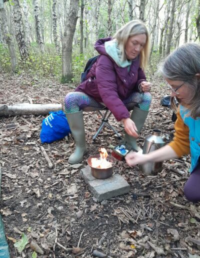 Craigmillar Community Grows: Two women are crouched round a small cooking fire in a woodland area