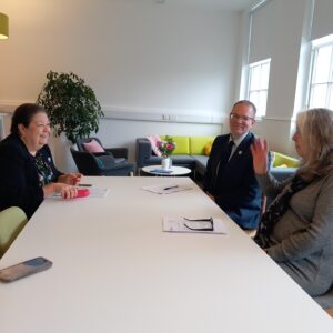 Jackie Baillie, Andrew Thomson and Lucy Wren sit at a white table, talking and smiling