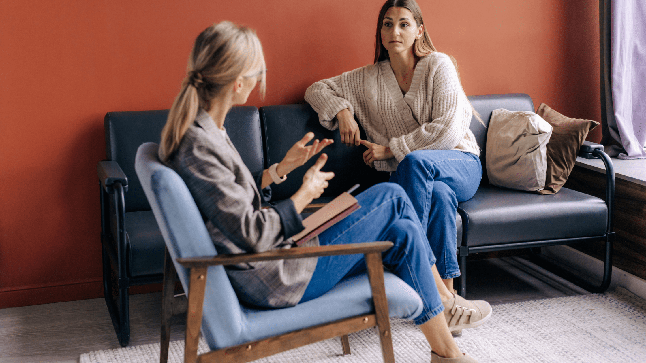 Counselling Service: A women sits on a couch talking to a women sitting on a chair next to her.