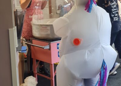 A woman dressed in an inflatable unicorn outfit is being given candy floss from a vendor.