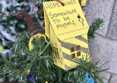 Close-up of a Christmas tree decorated with handmade ornaments, including a yellow paper house labeled "Somewhere to be Myself".