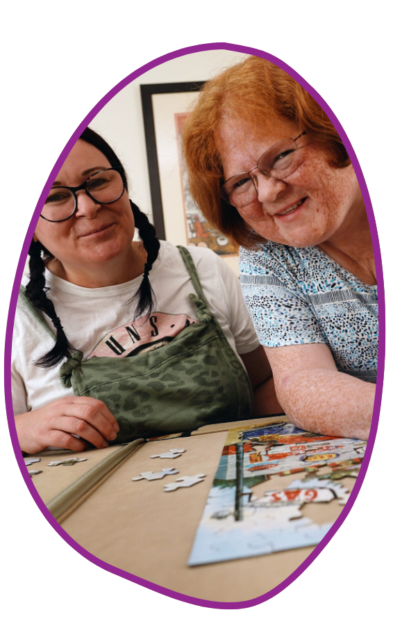 Glasgow Two women smile at the camera while doing a jigsaw puzzle.
