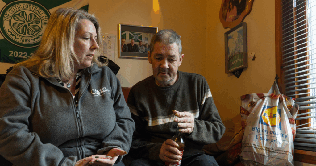 Heather from Argyll and Bute Housing Support sits beside Donnie on a couch in a casual environment. | Carr Gomm