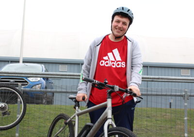 Person stands in a red t-shirt holding their bike. Smiling at the camera.