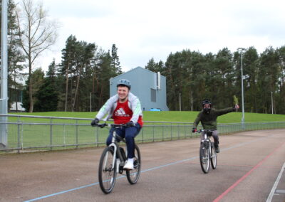 Two people ride bikes, one is pulling a thumbs up.