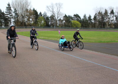 Four people riding bikes, one on a trike on a velodrome.