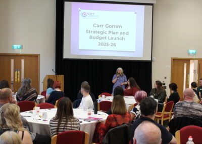 Person presents to a room. Title on the screen behind reads " Carr Gomm Strategic Plan and Budget Launch 2025/26