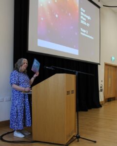 Person holds a copy of the Carr Gomm Strategic Plan while standing behind a lectern. 