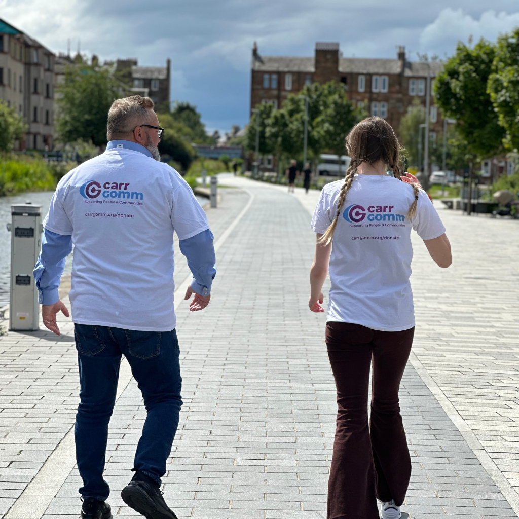 Greg, Chair of Board of Directors and Kat walk down a quiet street wearing Carr Gomm t-shirts. 