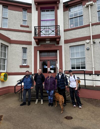 Group of five adults and a dog standing in front of a building with multiple doors and windows.