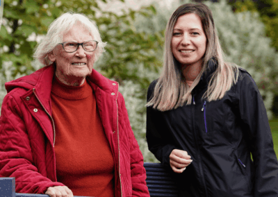 an older lady (Margaret) stands next to a young woman (Tina). They are smiling in a garden environment. | Carr Gomm Highland