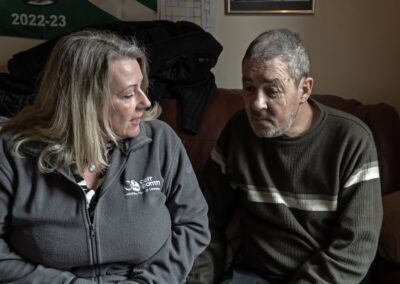 Two adults sitting and engaging in a conversation, with one wearing a logo-embroidered jacket and the other in a striped sweater.