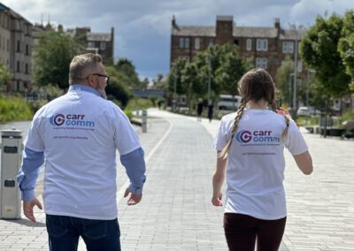 Two individuals walking along a city path, both wearing white shirts with "Carr Comm" logos on the back.