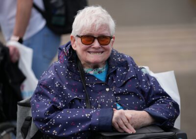 An older woman wearing a raincoat and sunglasses with a bright smile