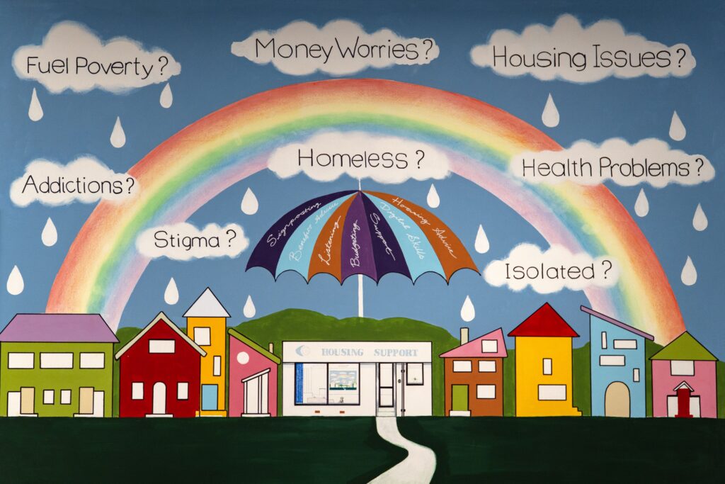 A colorful mural depicting a row of stylized houses under a large rainbow. Above the rainbow are the questions "Fuel Poverty?", "Money Worries?", "Housing Issues?", "Addictions?", "Homeless?", "Health Problems?", "Stigma?", "Isolated?" In the center, a large umbrella labeled "Counseling Support" shields the path leading to the houses, suggesting protection against these issues.