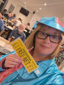 A person in a blue hat looks at the camera while holding a '£1 Free Bet' slip.