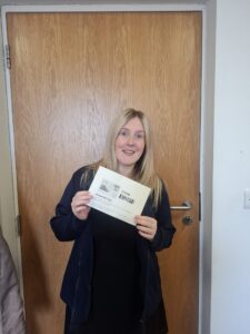 A person stands in front of a holding, posing for the camera while holding a certificate.