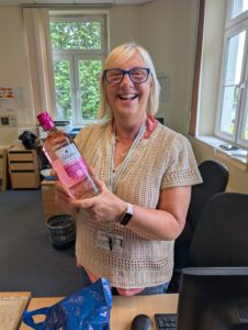 A person is smiling at the camera while holding a bottle of Gordon's Gin