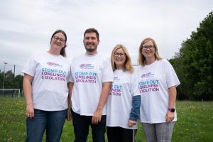 A group of 4 people in Carr Gomm shirts smile at the camera.