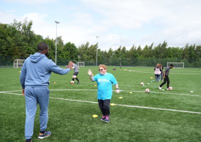 A woman in a blue Carr Gomm shirt high fives a man on a football pitch.