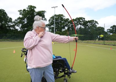 A woman in a pink hoody fires an arrow.