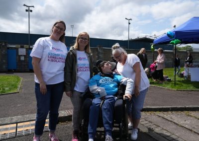 Three people in white Carr Gomm shirts and one person in a wheelchair, smile at the camera.