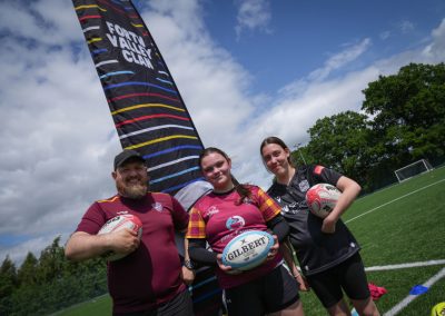 Three people wearing rugby shirts smile at the camera while holding a rugby ball.