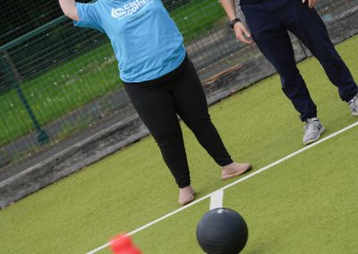 A women in a blue Carr Gomm shirt and a man in a black Health by Science shirt, stand on the grass and looking at a ball the women has thrown. She has her hands in the air.