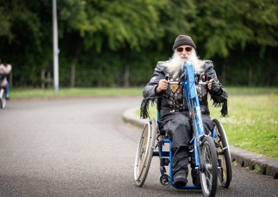 A man wearing a leather jacket, black hat and sunglasses rides an accessible bicycle.