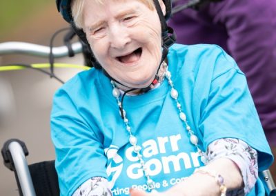 A women wearing a blue Carr Gomm shirt and cycle helmet smiles and claps her hands.