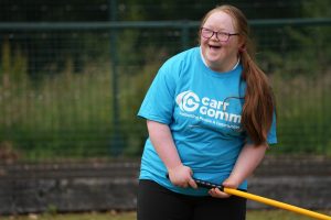 A women with a blue Carr Gomm shirt and red hair, is laughing while holding a sports stick.
