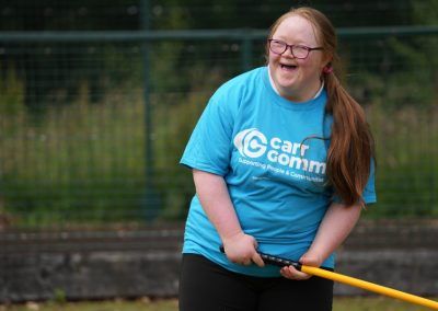 A women with a blue Carr Gomm shirt and red hair, is laughing while holding a sports stick.