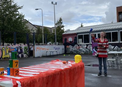 Carr Gomm Glasgow Forum - Outside a table with a red cloth is set up with cans. A women is throwing a bean bag at them.