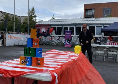 Carr Gomm Glasgow Forum - Outside a table with a red cloth is set up with cans. A man is throwing a bean bag at them.