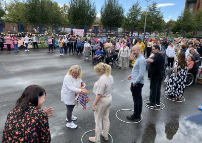 Carr Gomm Glasgow Forum - A row of people are standing holding spoons. A women is giving them eggs from a plastic bag. A group of people can be seen to be watching.